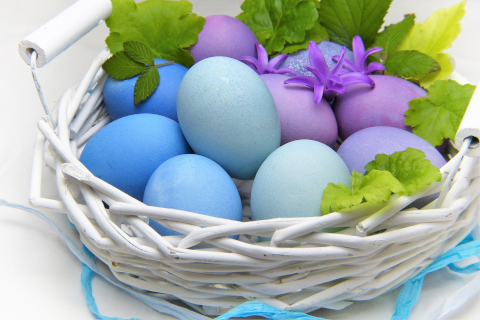 A white wicker basket filled with blue and purple Easter eggs