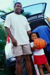 A father standing with his daughter who is holding a basketball